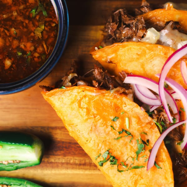 Birria tacos with red onions and cilantro, served with a side of consommé and jalapeños.