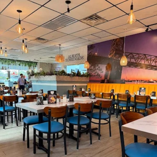 Brightly lit Amanecer Cocina y Cafe dining room with blue chairs, yellow booths, and a bridge mural.