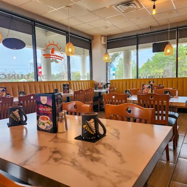 Interior of Amanecer Cocina y Cafe with empty tables, yellow booths, and large windows.