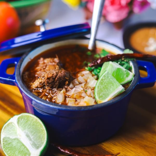 Amanecer Cocina y Cafe's birria in a blue pot, garnished with cilantro, onions, and lime.