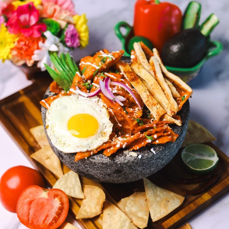 Amanecer Cocina y Cafe's chilaquiles with a fried egg, avocado, and tortilla chips on a wooden board.