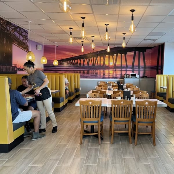 A server attends to customers in a bright, modern restaurant with a large sunset bridge mural.