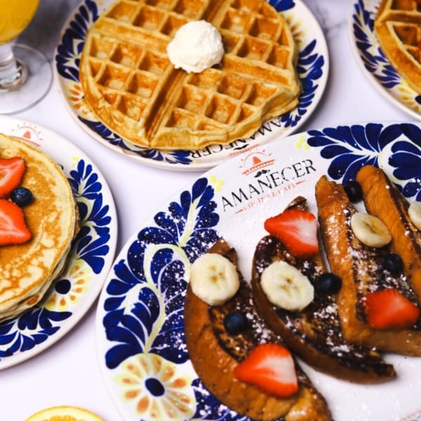 Amanecer Cocina y Cafe breakfast spread with waffles, pancakes, and French toast on decorative plates.