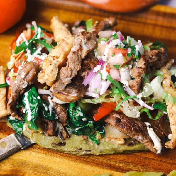 Amanecer Cocina y Cafe's breakfast dish with steak, chicken, vegetables, and crema on a wooden board.