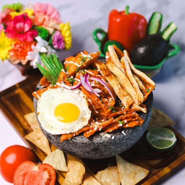 Amanecer Cocina y Cafe's chilaquiles with a fried egg, red onions, and avocado in a stone bowl.