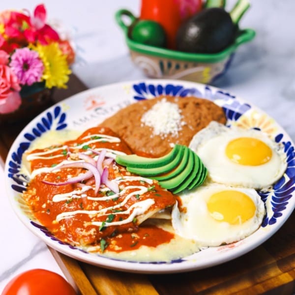 Amanecer Cocina y Cafe's chilaquiles with red sauce, two fried eggs, refried beans, and avocado slices.