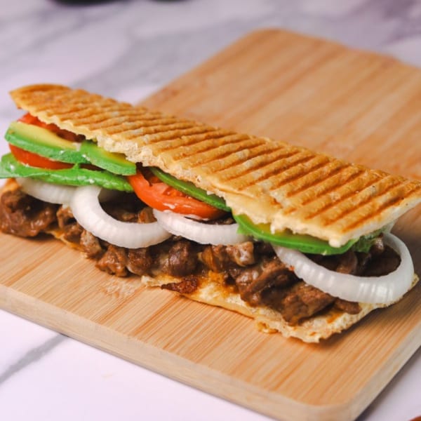 Amanecer Cocina y Cafe's breakfast panini with steak, onions, tomatoes, and avocado on a wooden board.