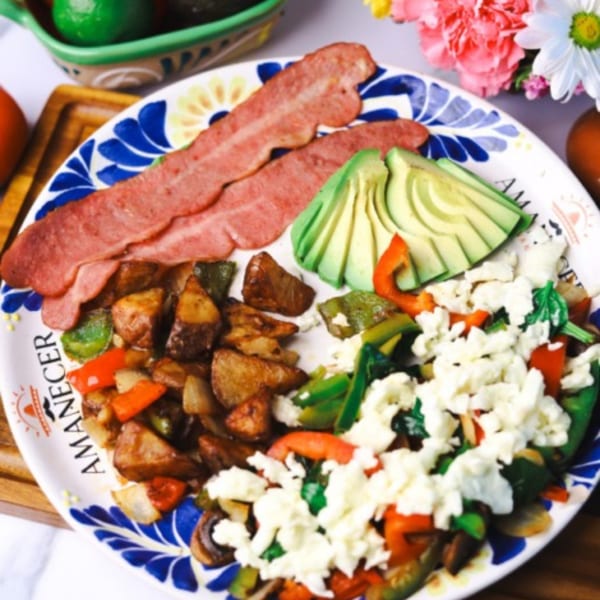 Amanecer Cocina y Cafe breakfast plate with bacon, avocado, potatoes, and scrambled eggs with vegetables.