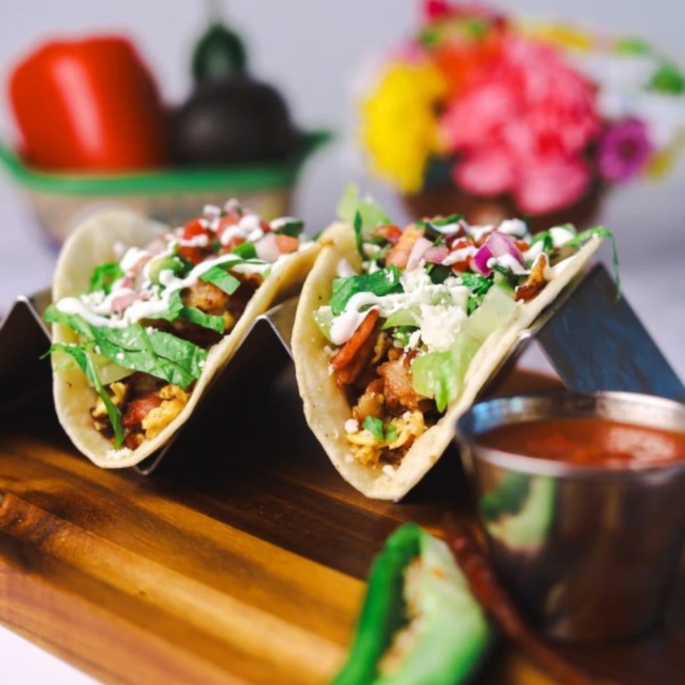 Two breakfast tacos with scrambled eggs, bacon, lettuce, cheese, and salsa on a wooden board.